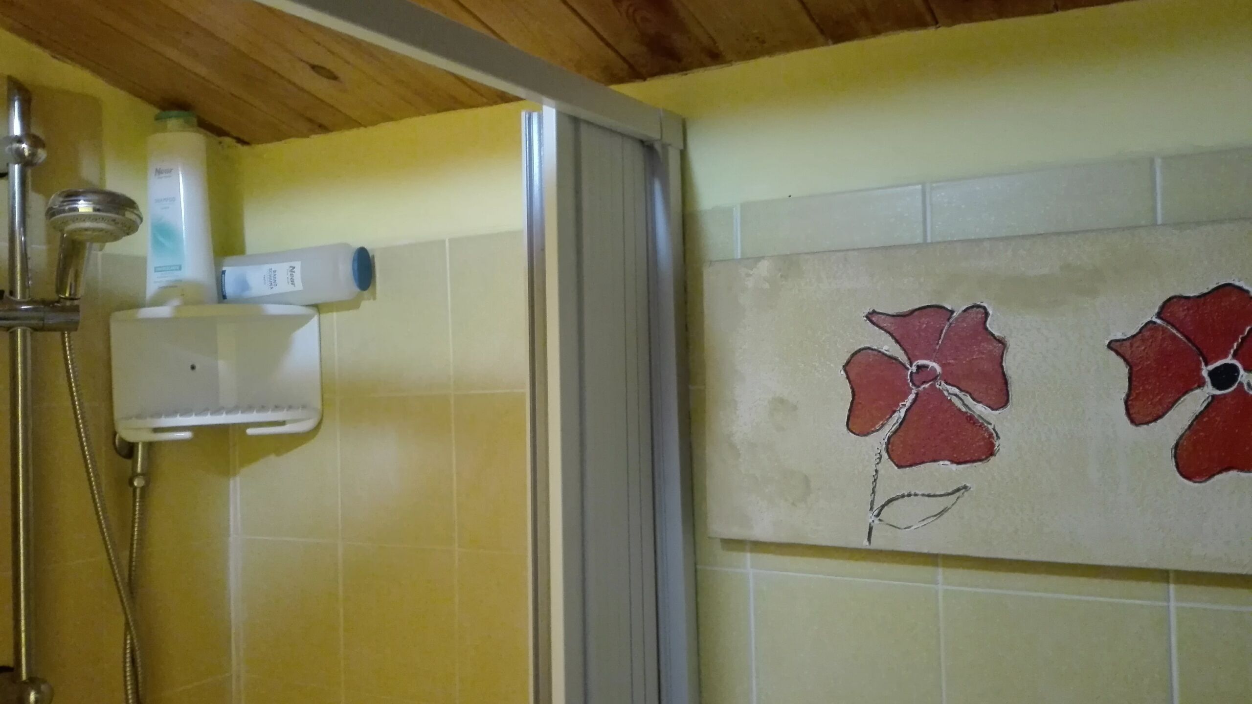 Un baño con baldosas amarillas, una ducha, dispensador de jabón en la pared y un diseño de baldosas con motivos florales.