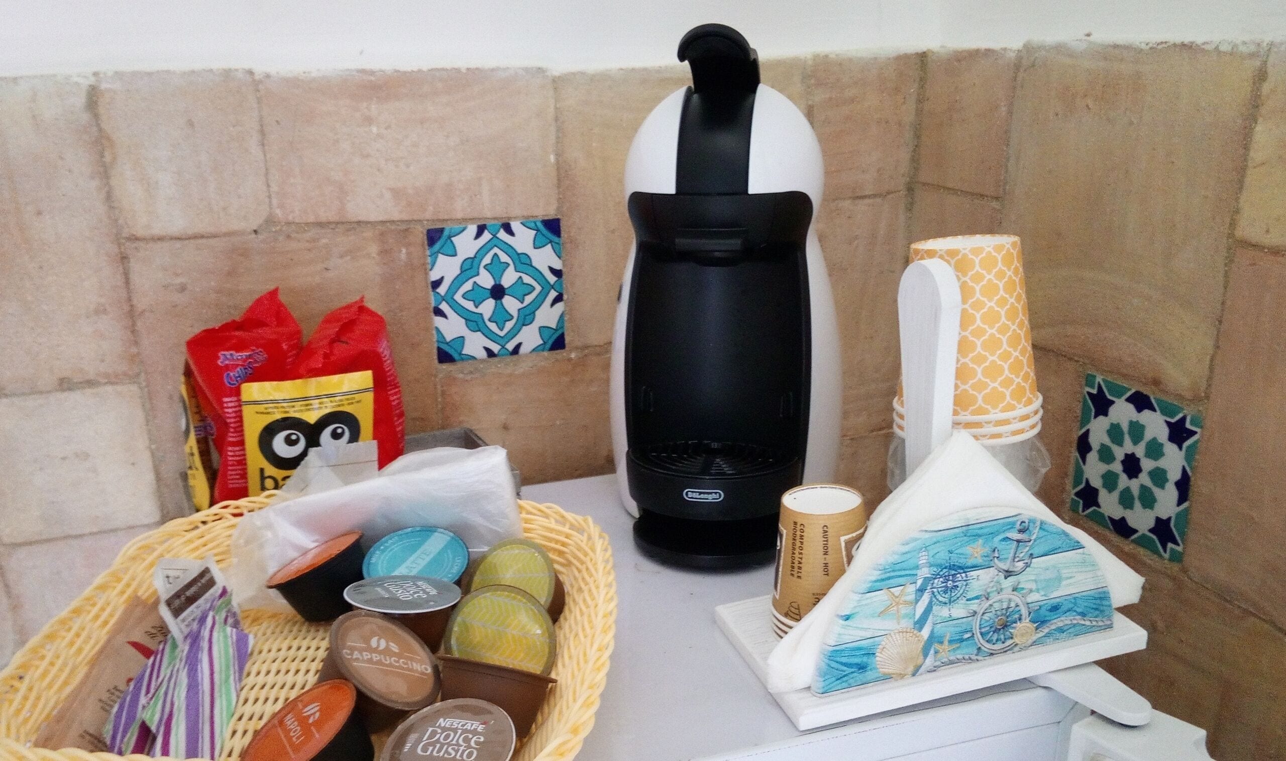 A kitchen area with a coffee maker, a basket of coffee pods, a coffee cup, and a decorative item on the counter.