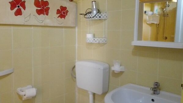 Un baño con azulejos amarillos, un inodoro, un lavabo y un espejo.