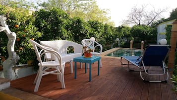 A wooden deck with wicker furniture, a small table with a potted plant, and a pool area.