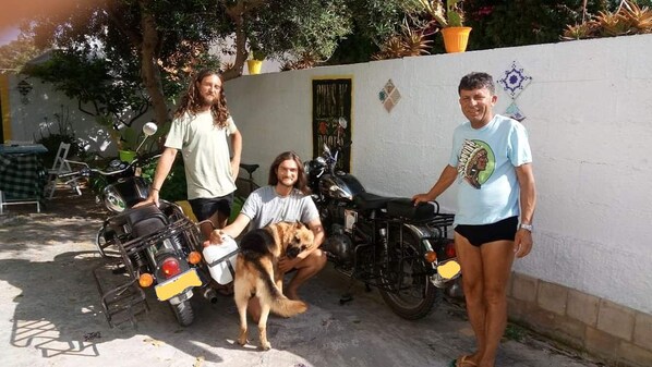 A group of people with motorcycles and a dog in a courtyard with a white wall and potted plants. - Zagara di Sicilia (Marsala)