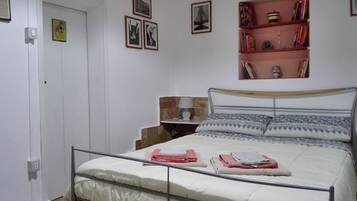 Un dormitorio con cama, mesita de noche, lámpara y estantería.