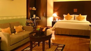 A hotel room with a bed, a sofa, a small table, and a nightstand with a lamp. - Hotel Pacific Balikpapan (Balikpapan)