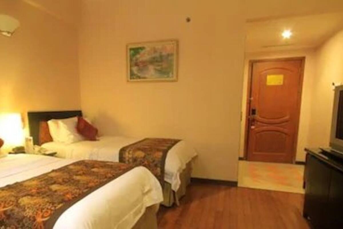 Ein Hotelzimmer mit zwei Betten, einem Fernseher, einem Bild an der Wand und einer Tür.
