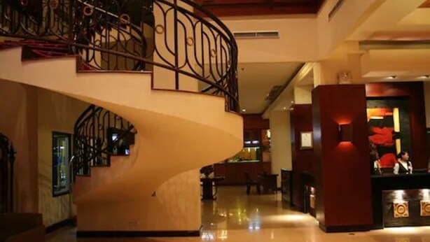 A hotel lobby with a curved staircase, a reception desk, and a decorative wall. - Hotel Pacific Balikpapan (Balikpapan)