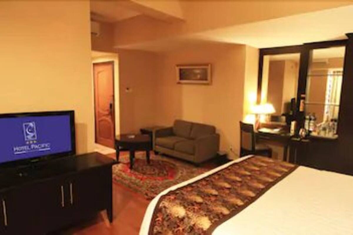Ein Hotelzimmer mit einem Bett, einem Fernseher, einem Sofa, einem Schreibtisch und einem Spiegel.