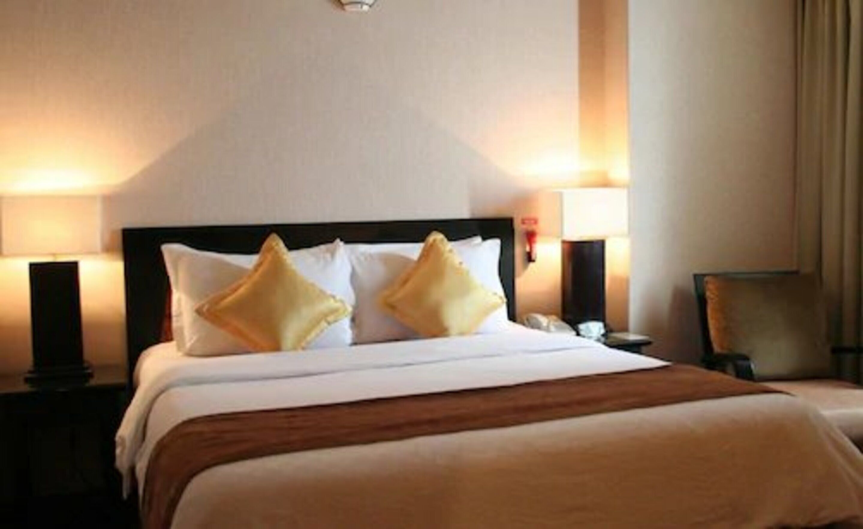 A hotel room with a large bed, two bedside lamps, and a nightstand.
