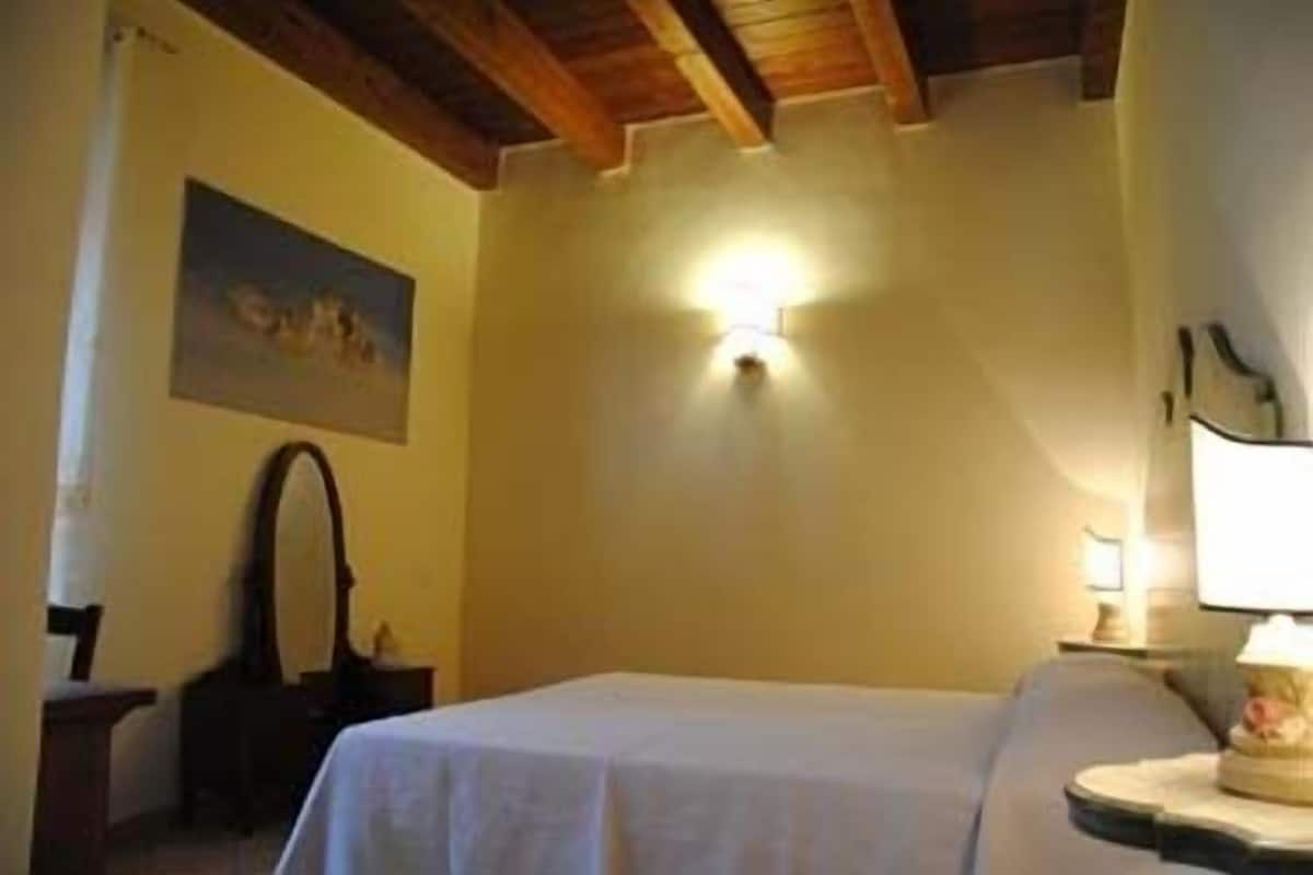 Ein Zimmer mit einem Bett, einer Wandleuchte, einem Gemälde und einem Nachttisch mit Lampe.