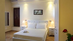 A bedroom with a large bed, two bedside tables, a nightstand, a door, and a wall-mounted picture. - Palazzo Madeo - Residenza d'Epoca (Crosia)