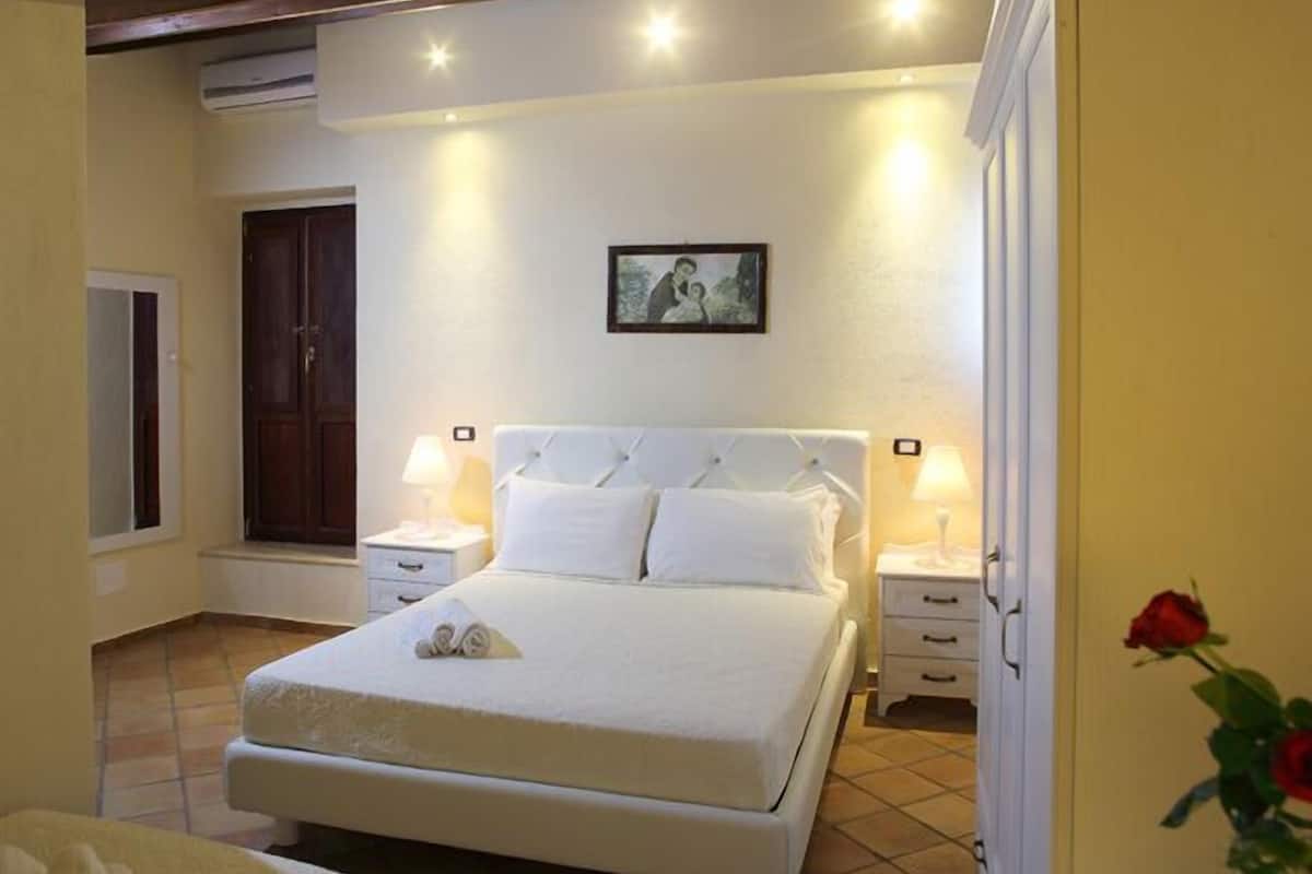Ein Schlafzimmer mit einem großen Bett, zwei Nachttischen, einem Beistelltisch, einer Tür und einem Wandbild.
