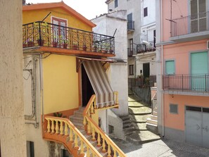 A narrow street with buildings on either side, featuring balconies with railings and potted plants. - Palazzo Madeo - Residenza d'Epoca (Crosia)