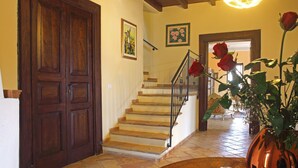 A staircase with wooden steps and a metal railing, leading to a room with a large wooden door and a vase with roses. - Palazzo Madeo - Residenza d'Epoca (Crosia)