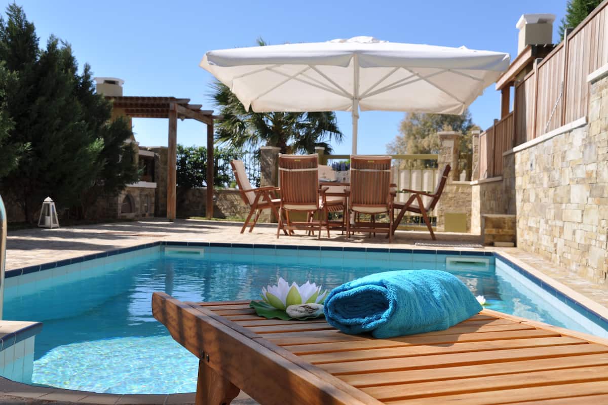 A poolside area with a wooden lounge chair, a rolled-up towel, and a white umbrella.