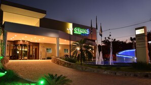 Ein Hotel Eingang mit einem Schild mit der Aufschrift 'OTHON SUITES', einer Fontäne und einer gut beleuchteten Auffahrt.