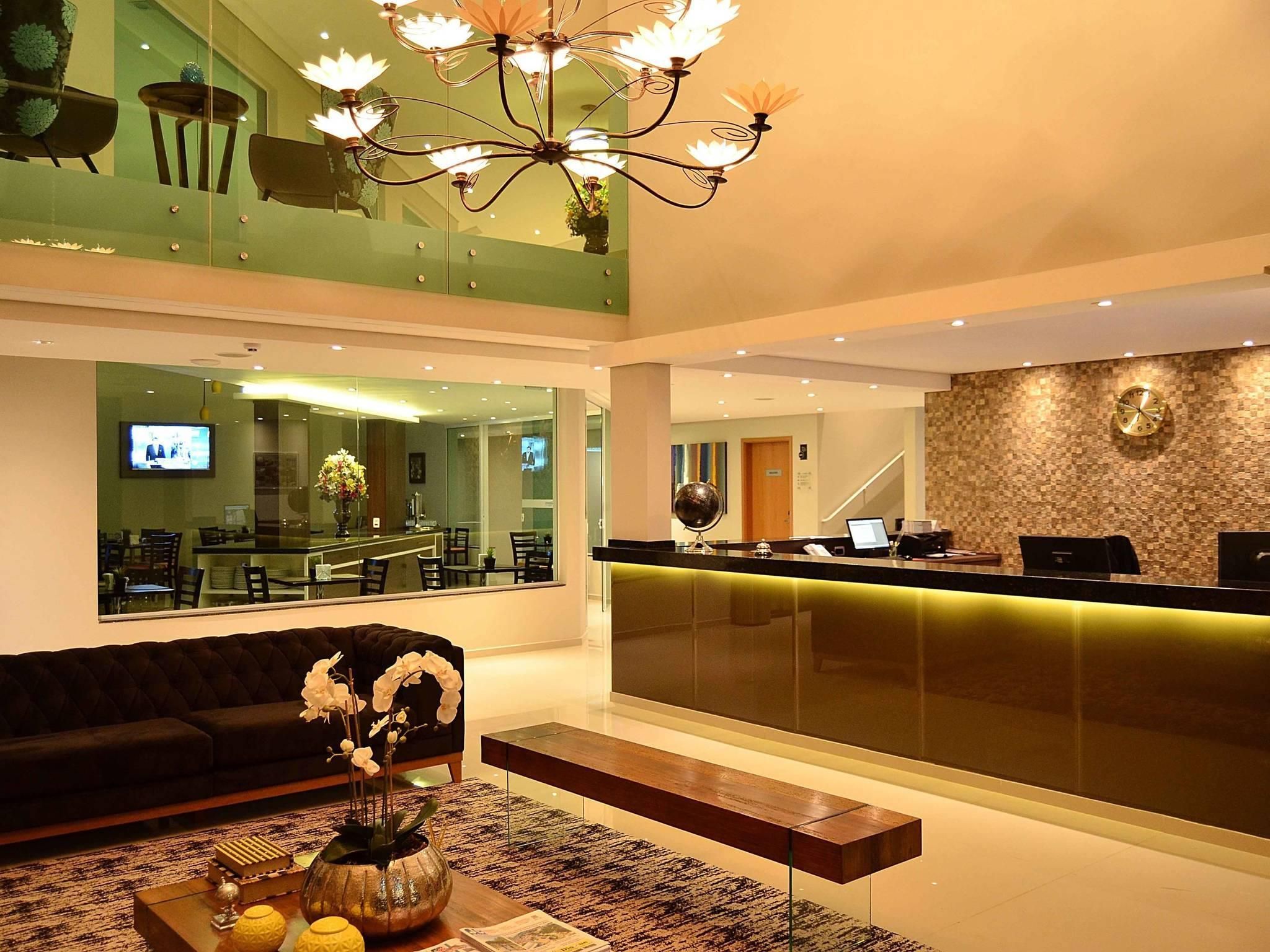 A hotel lobby with a reception desk, a sofa, a coffee table with flowers, and a television screen.