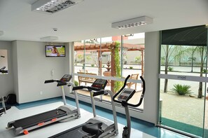 Une salle de sport équipée de tapis de course, d’un téléviseur et de grandes fenêtres donnant sur une cour intérieure.