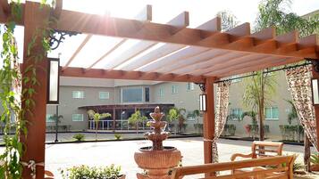 Un espacio al aire libre techado con un banco de madera, una fuente escalonada y plantas en macetas.