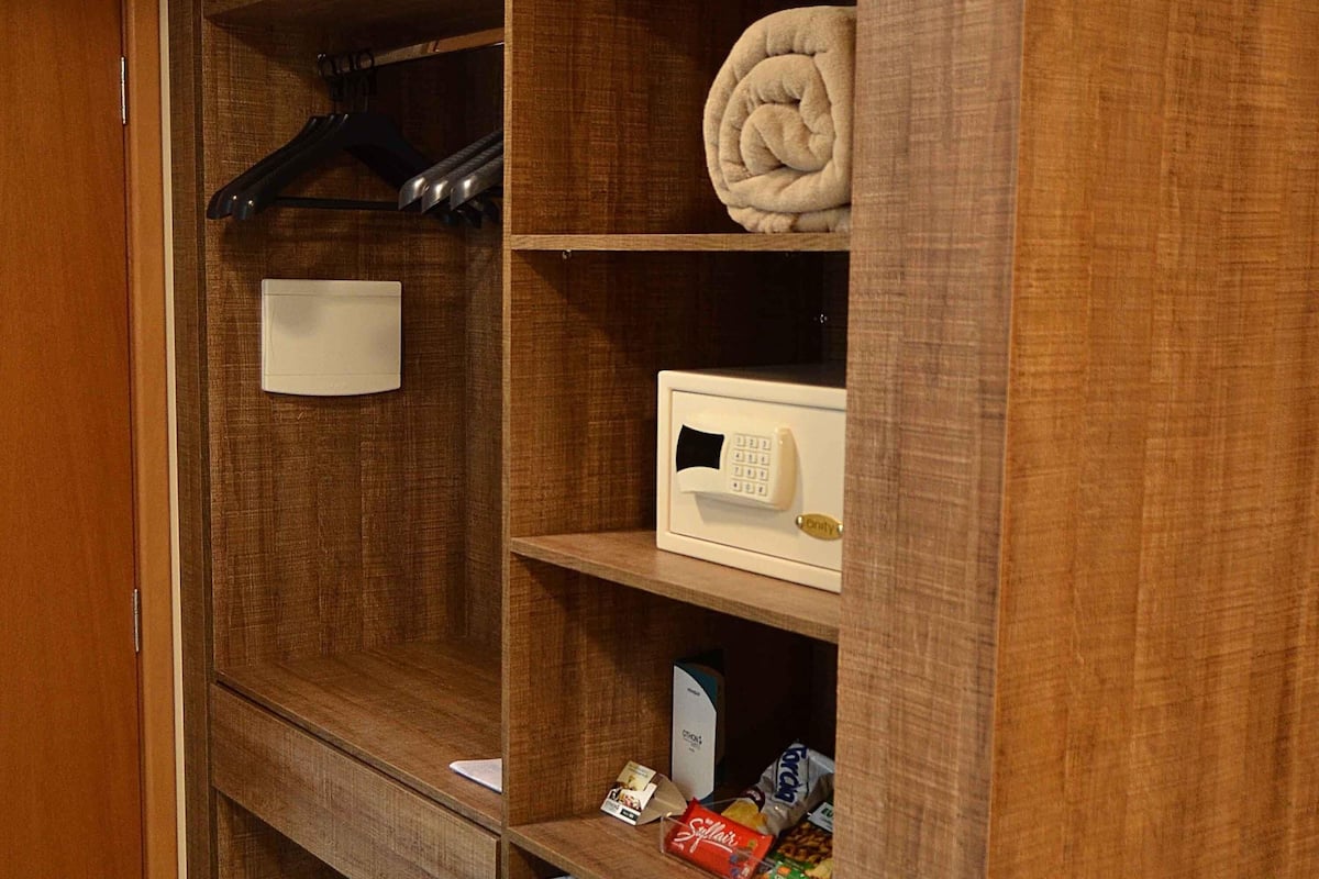 Um guarda-roupa de madeira com um termostato branco, uma toalha dobrada e um casaco preto pendurado.