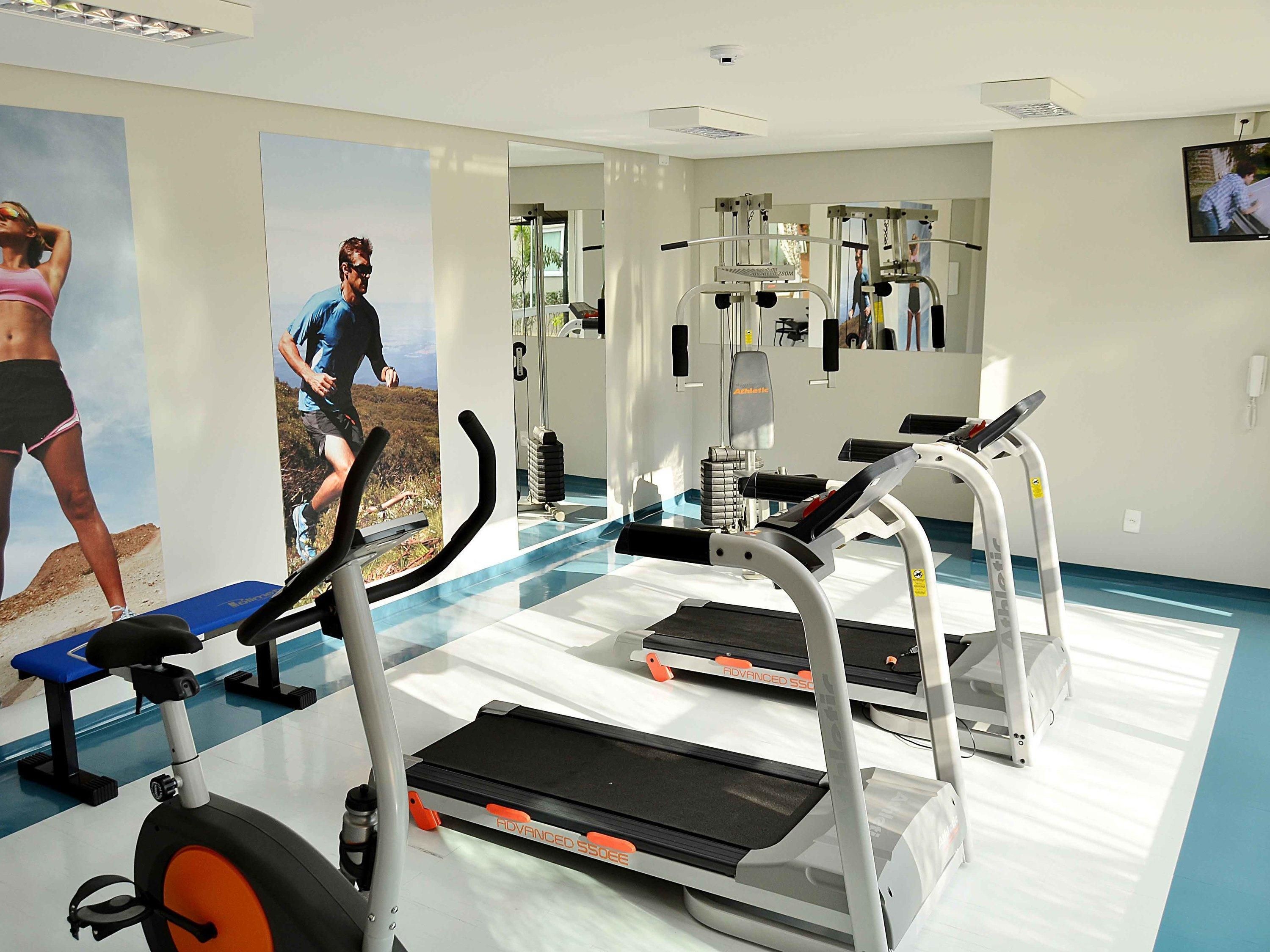 Un gimnasio con cintas de correr, elípticas y un espejo grande.