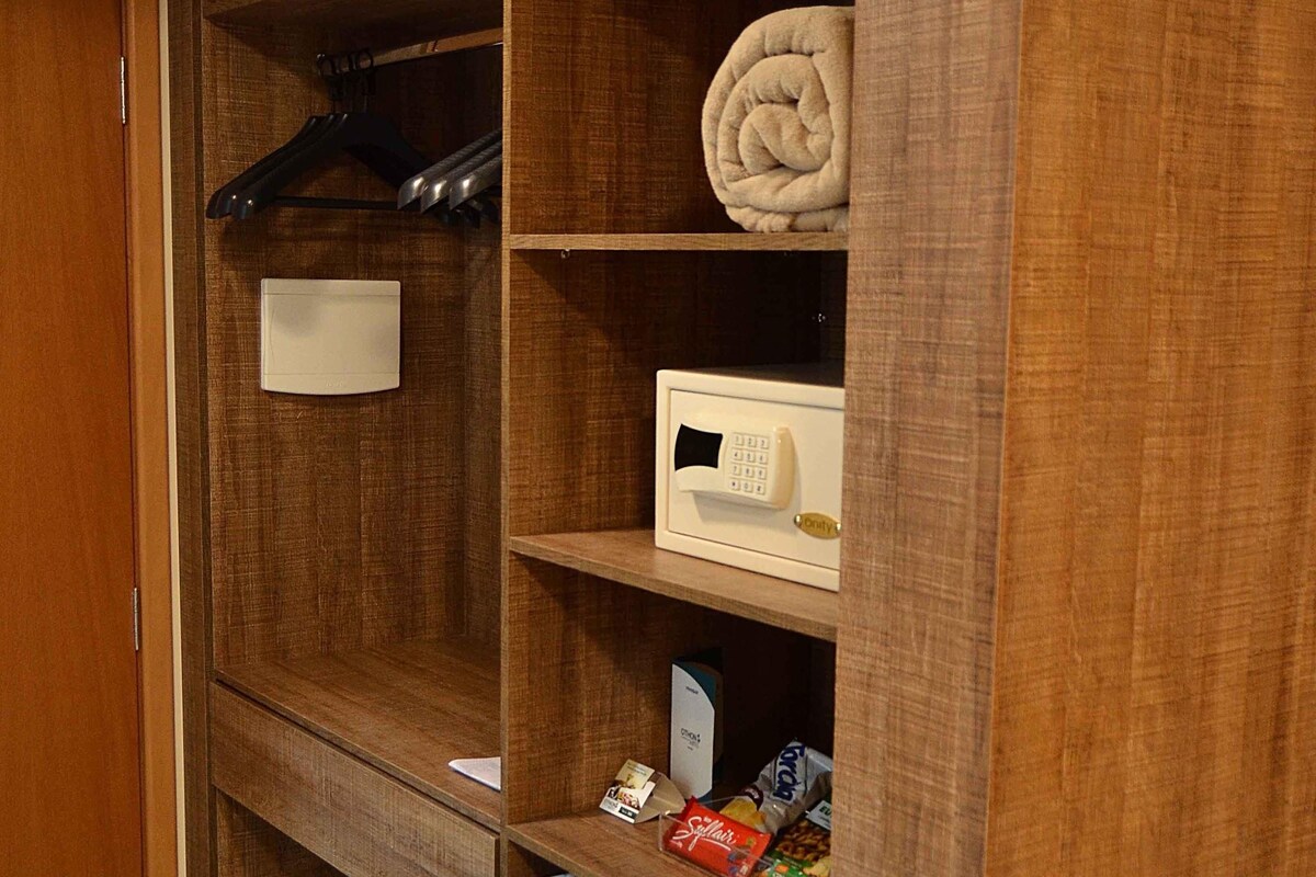 Une armoire en bois avec un thermostat blanc, une serviette pliée et une veste noire suspendue.