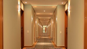 Un couloir d'hôtel avec des revêtements de sol en moquette, des portes en bois et des luminaires fixés au mur.