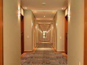 A hotel hallway with carpeted floors, wooden doors, and wall-mounted lighting.