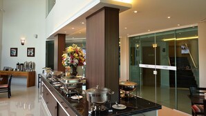 A modern hotel lobby with a buffet setup, a staircase, and a glass wall.