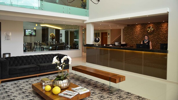 A modern hotel lobby with a black sofa, a reception desk, and a large mirror reflecting the interior.