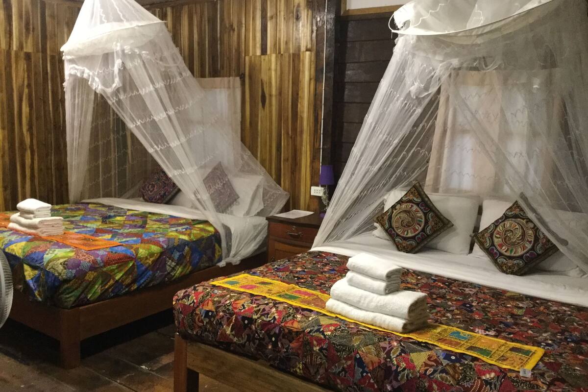 Zwei Betten mit bunten Quilts und weißen Handtüchern, jeweils mit Baldachin.