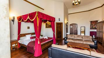 Un dormitorio con una cama con dosel, una zona de estar con sofá y mesa de centro, suelo de madera y un candelabro.
