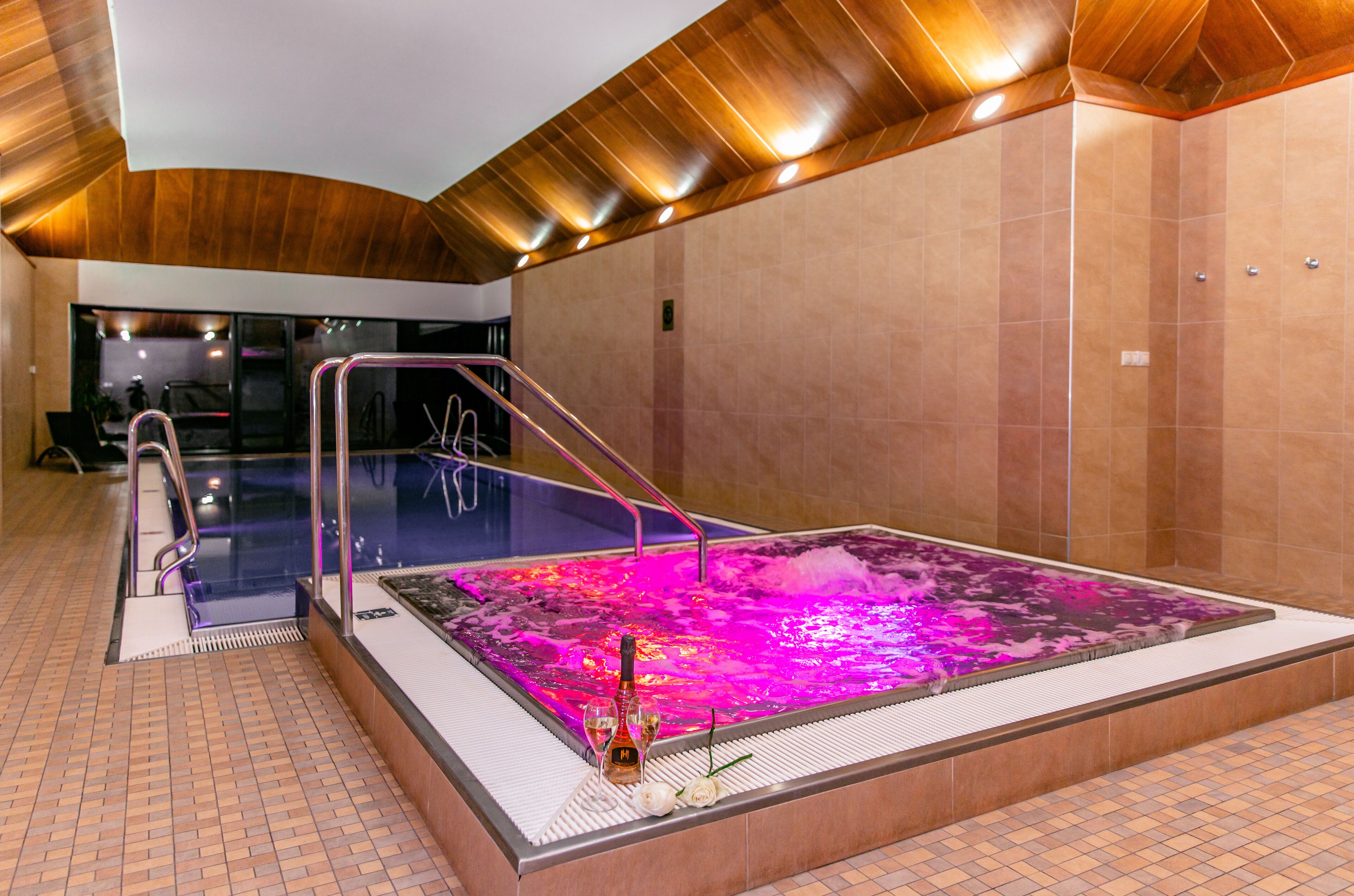A spa area with a hot tub, a glass-enclosed pool, and a wooden ceiling.