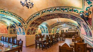 A restaurant with ornate, colorful ceiling designs and wooden tables and chairs.