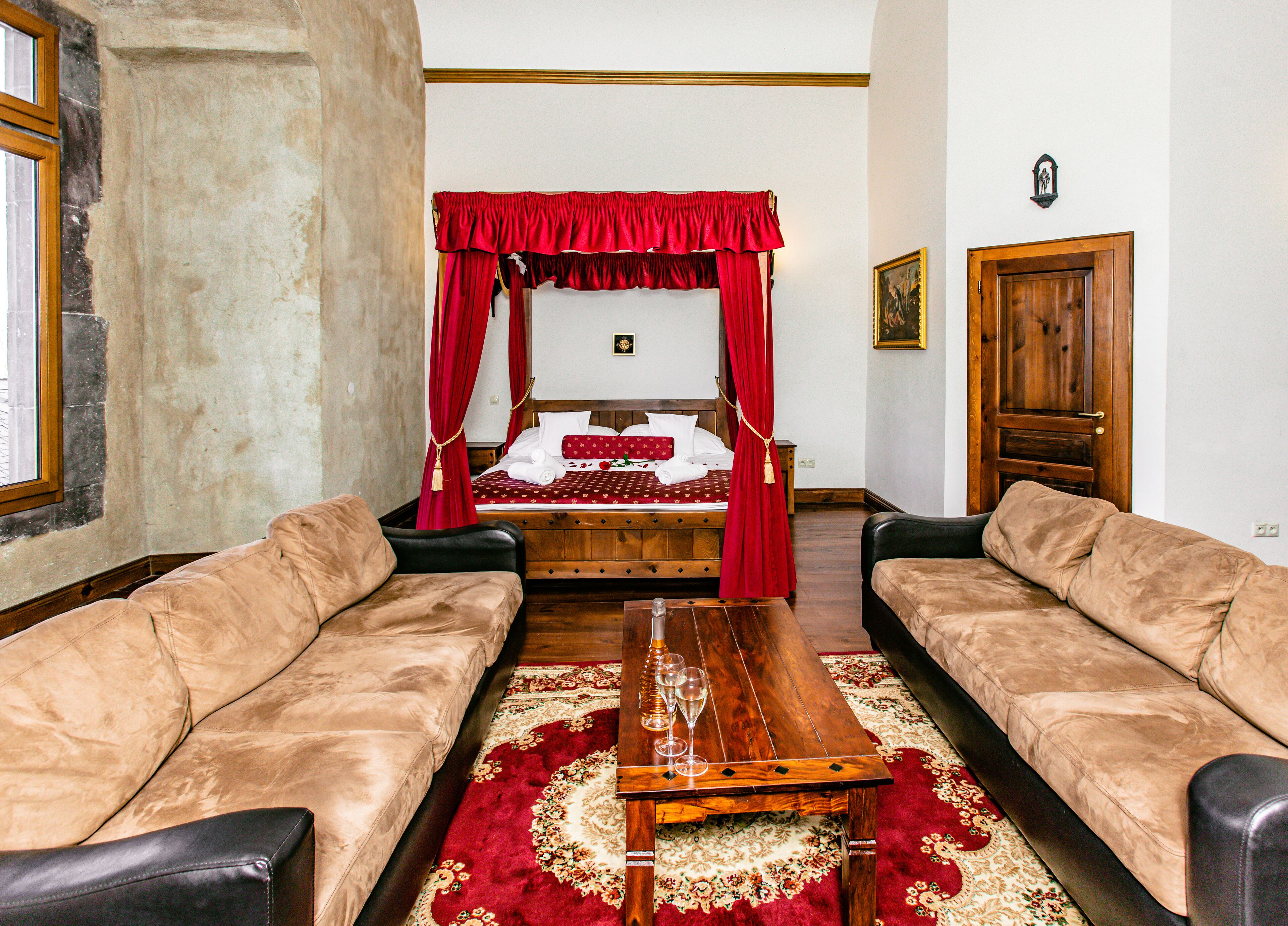 Un dormitorio con una cama con dosel, dos sofás de cuero, una mesa de centro de madera y una alfombra roja.