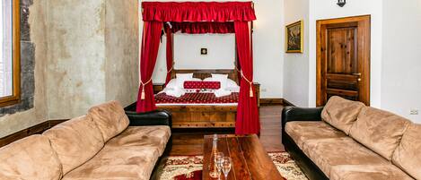 Un dormitorio con una cama con dosel, dos sofás de cuero, una mesa de centro de madera y una alfombra roja.