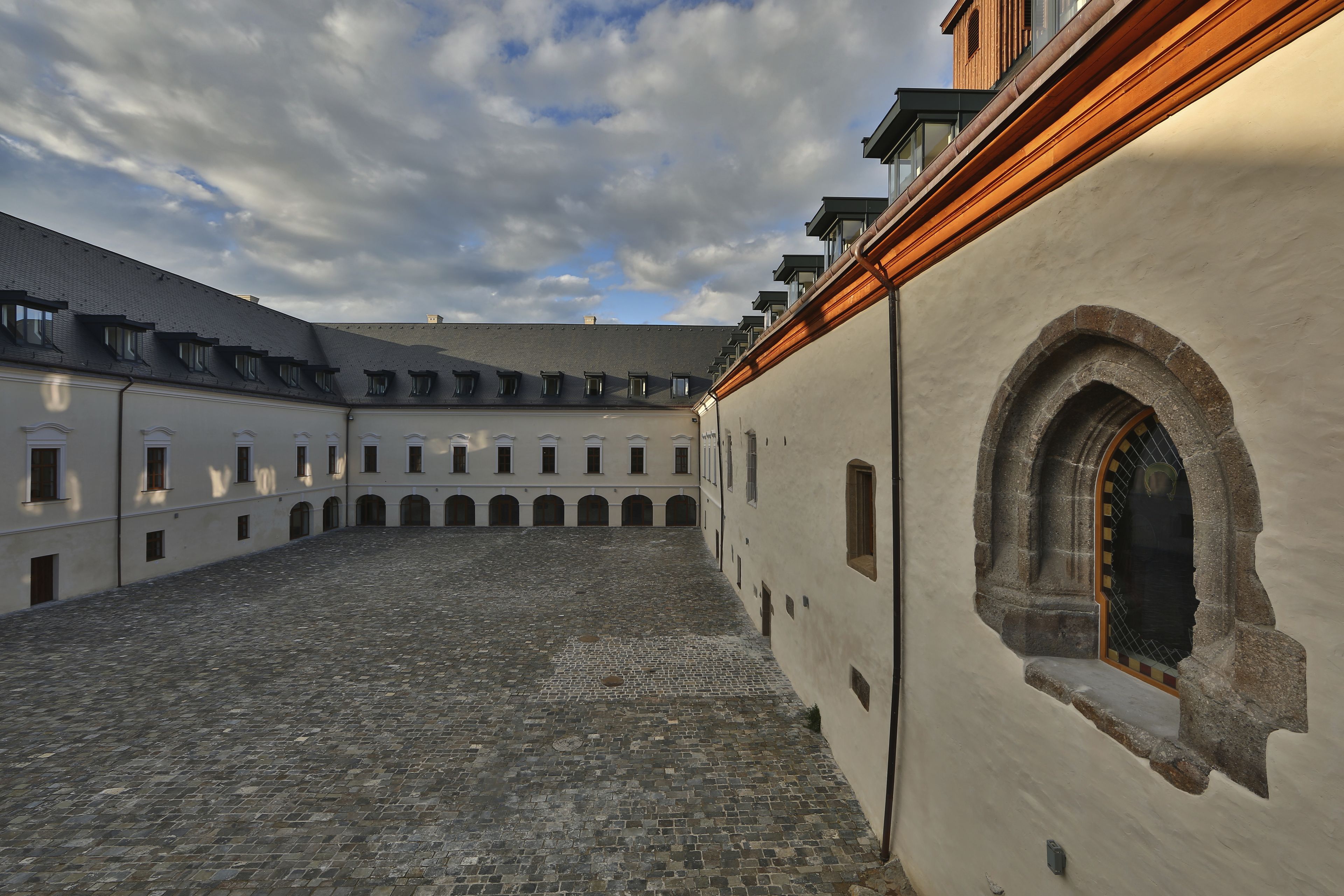 A courtyard with cobblestone flooring, a large arched window, and a building with multiple balconies.