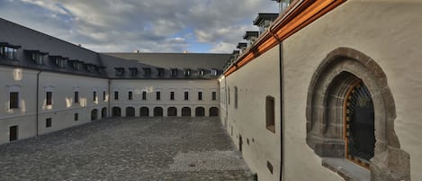 A courtyard with cobblestone flooring, a large arched window, and a building with multiple balconies.