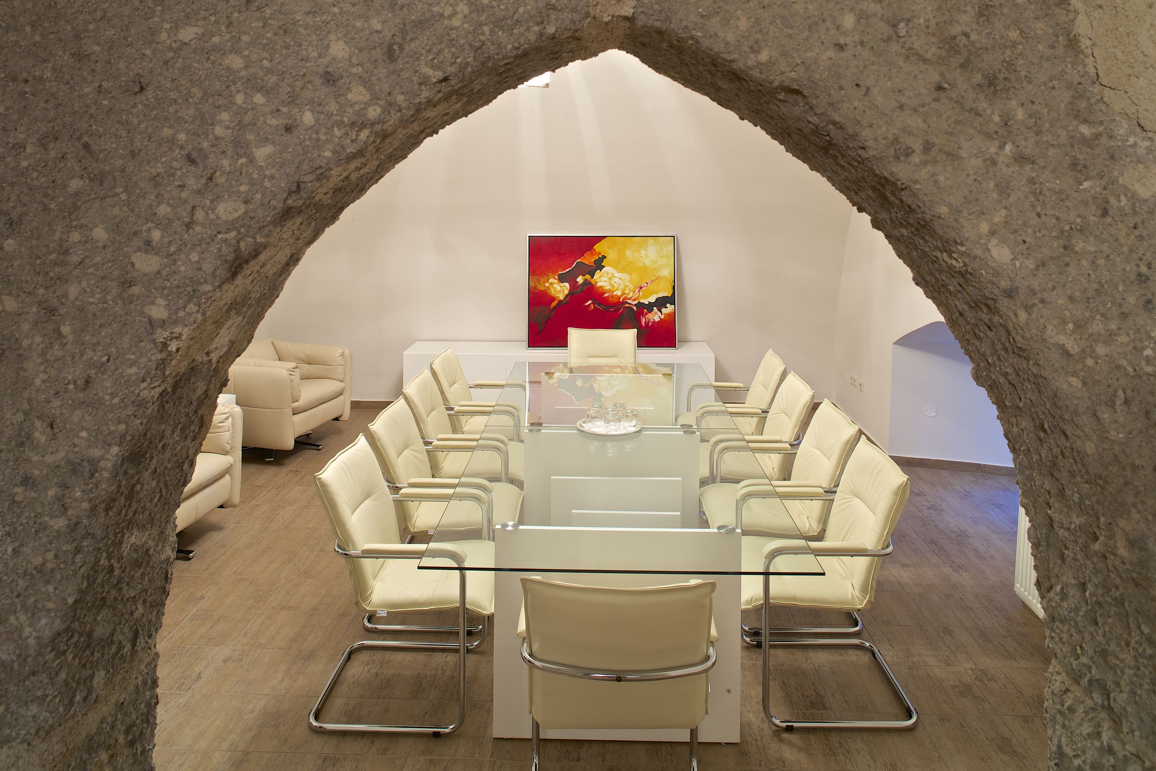 A conference room with a glass table, white chairs, a sofa, and a painting on the wall.