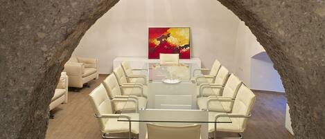 A conference room with a glass table, white chairs, a sofa, and a painting on the wall.