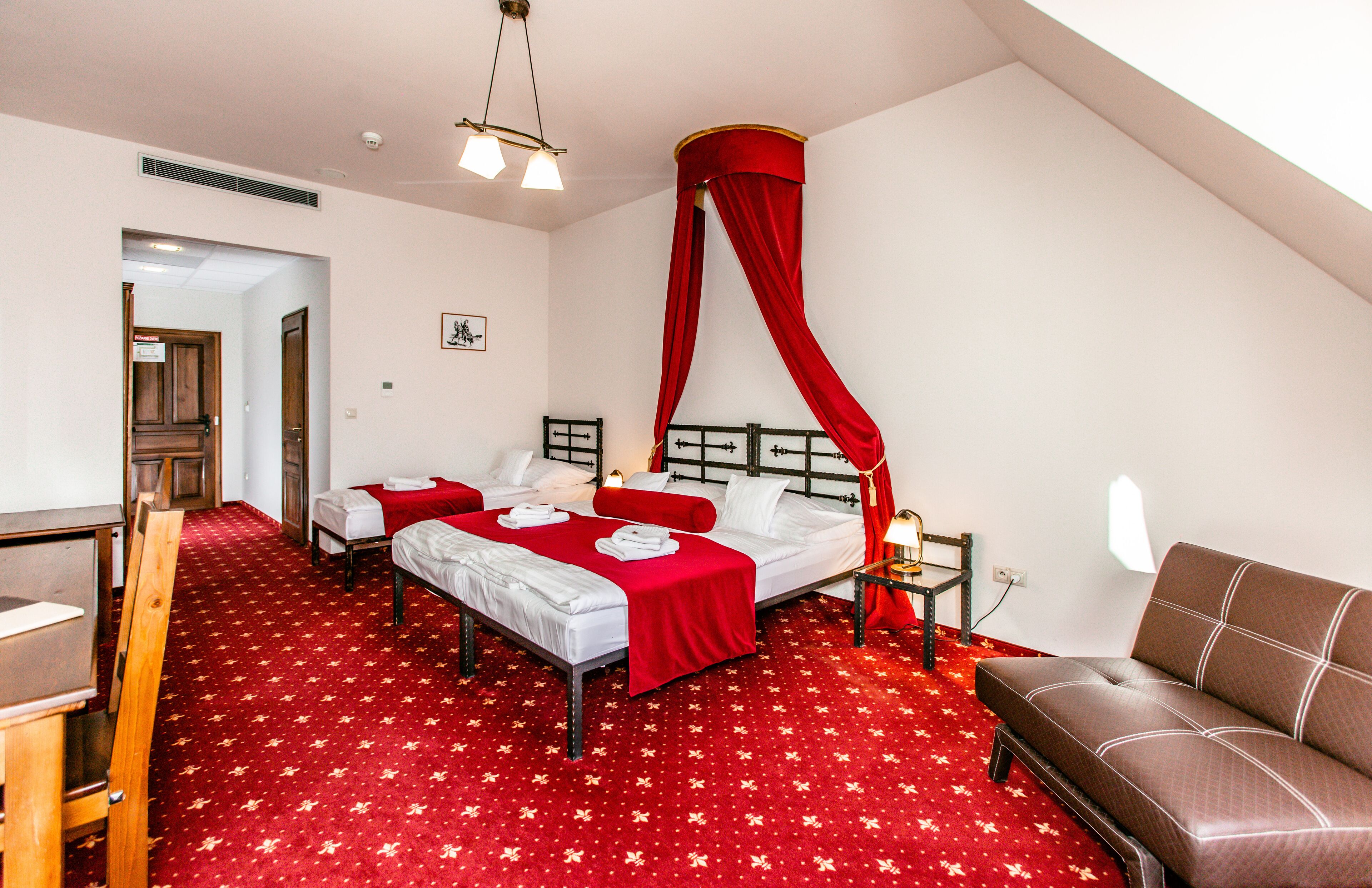 A hotel room with two beds, a sofa, a desk, and a red canopy bed.
