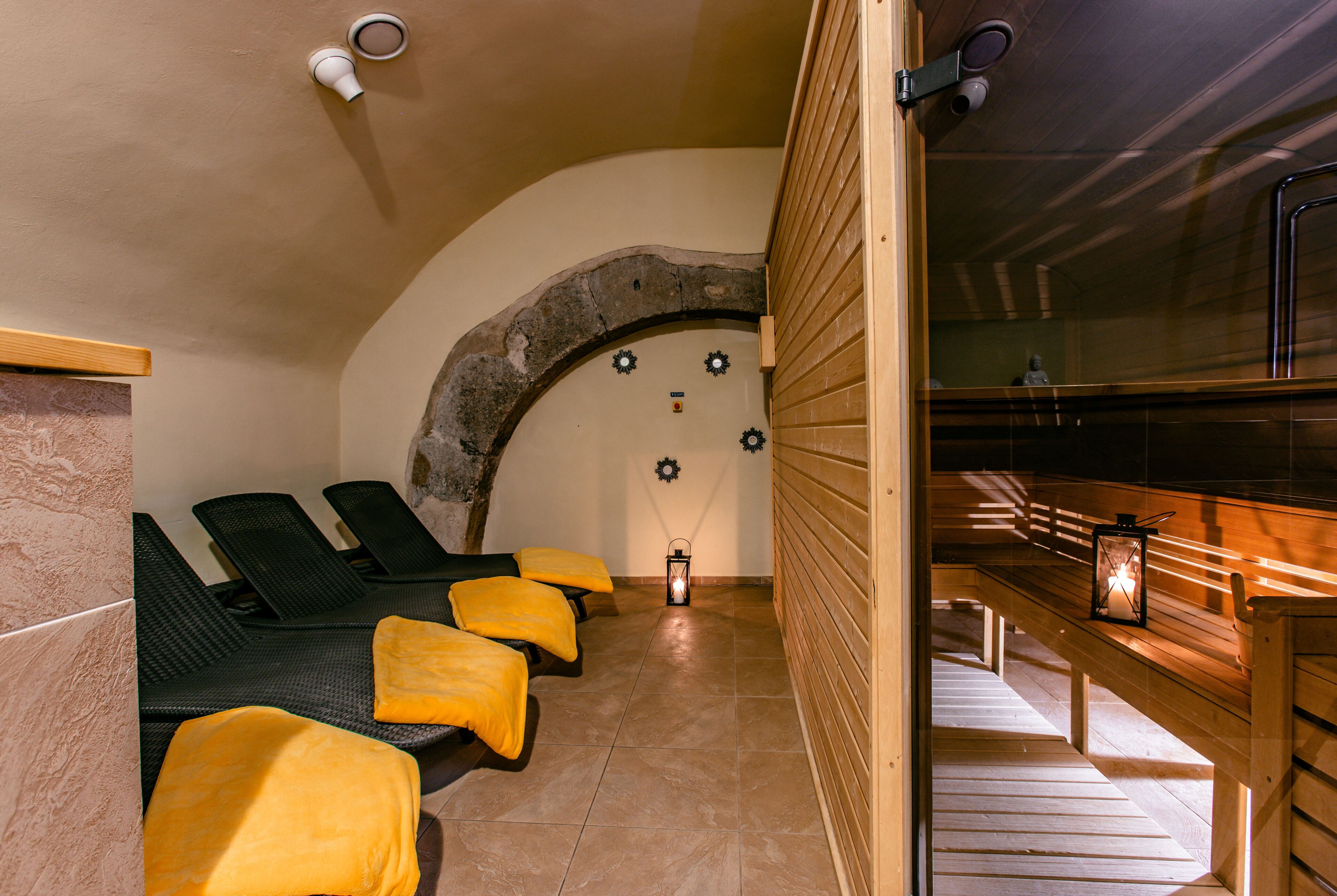 Una sauna con bancos de madera y toallas amarillas, un arco de piedra y una pared de madera con un banco y un farol.