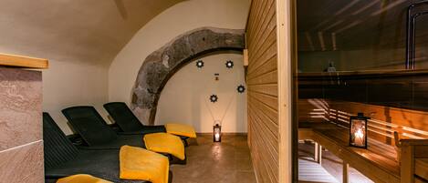 Una sauna con bancos de madera y toallas amarillas, un arco de piedra y una pared de madera con un banco y un farol.