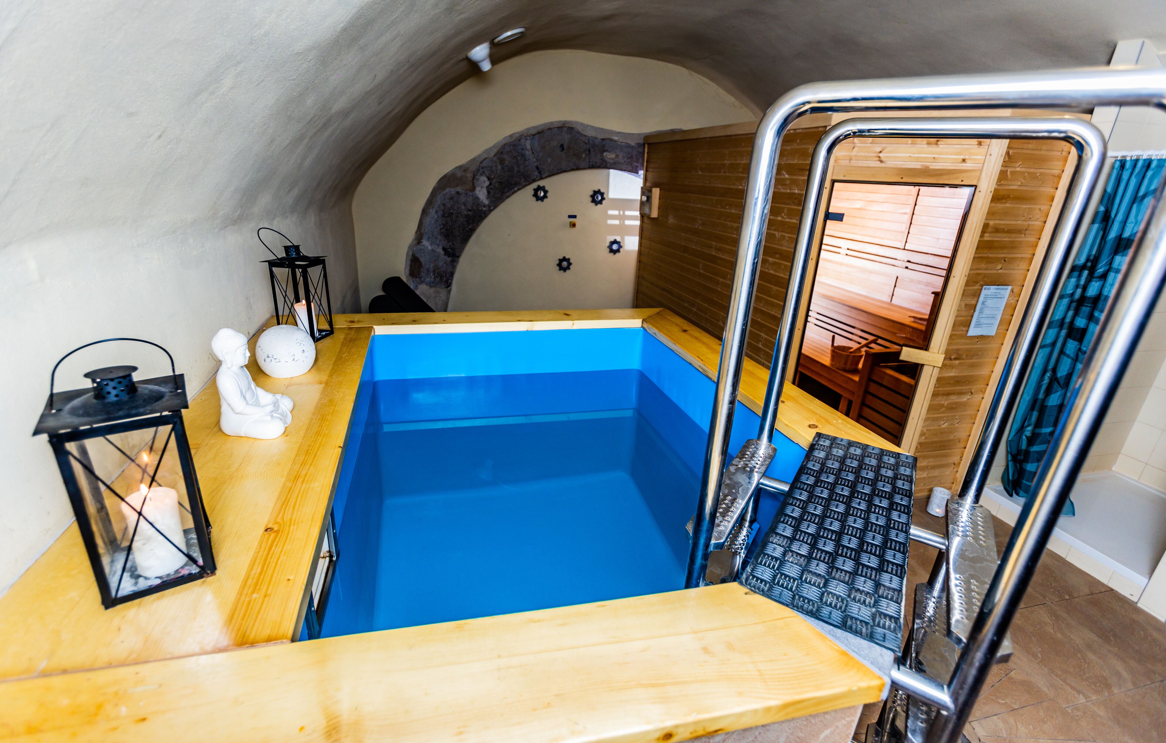 A small, cozy room with a wooden floor, a blue bathtub, a white bust sculpture, and a black lantern.
