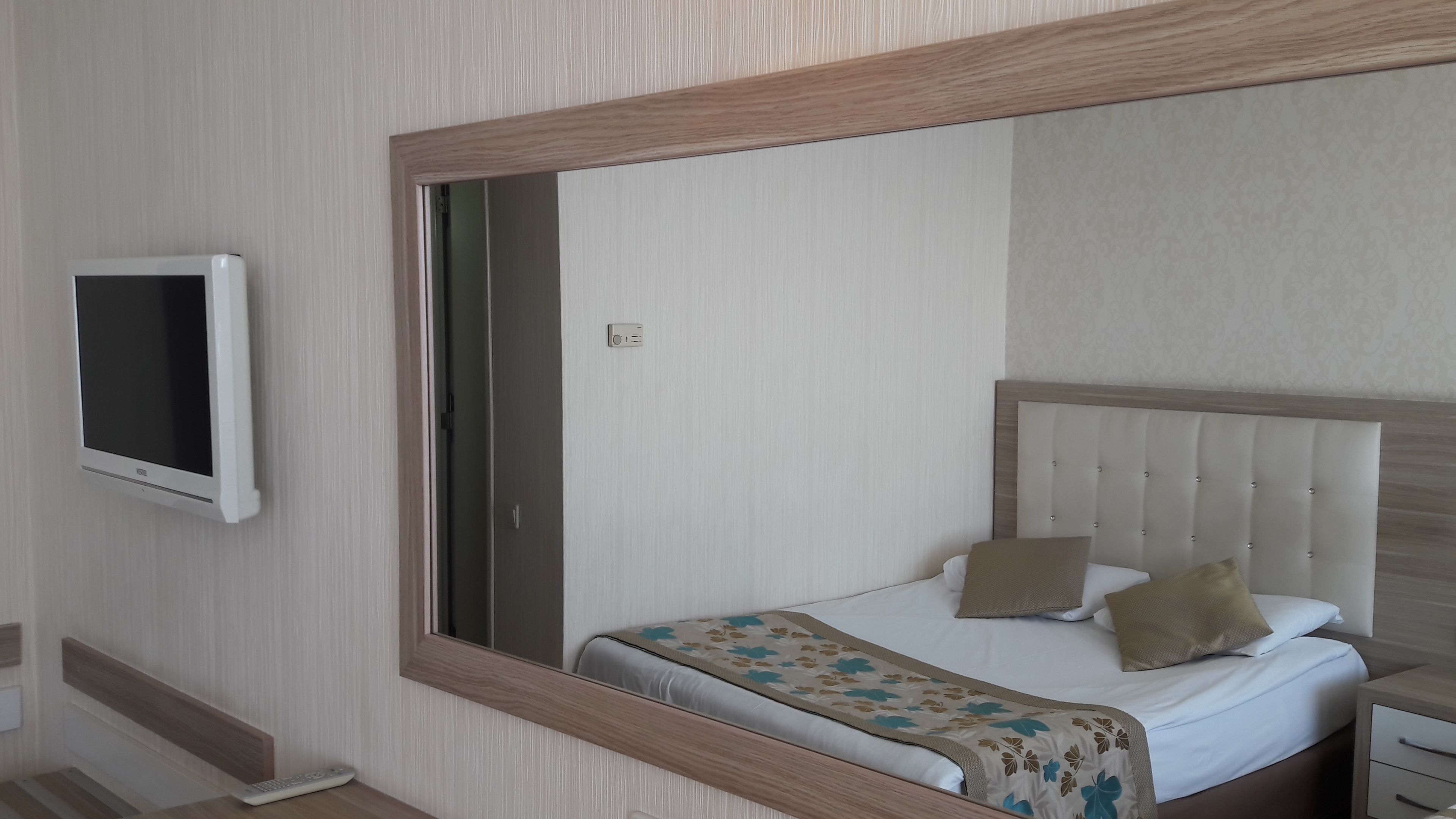 Habitación de hotel con una cama, una mesita de noche, un televisor montado en la pared y un espejo grande sobre la cama.