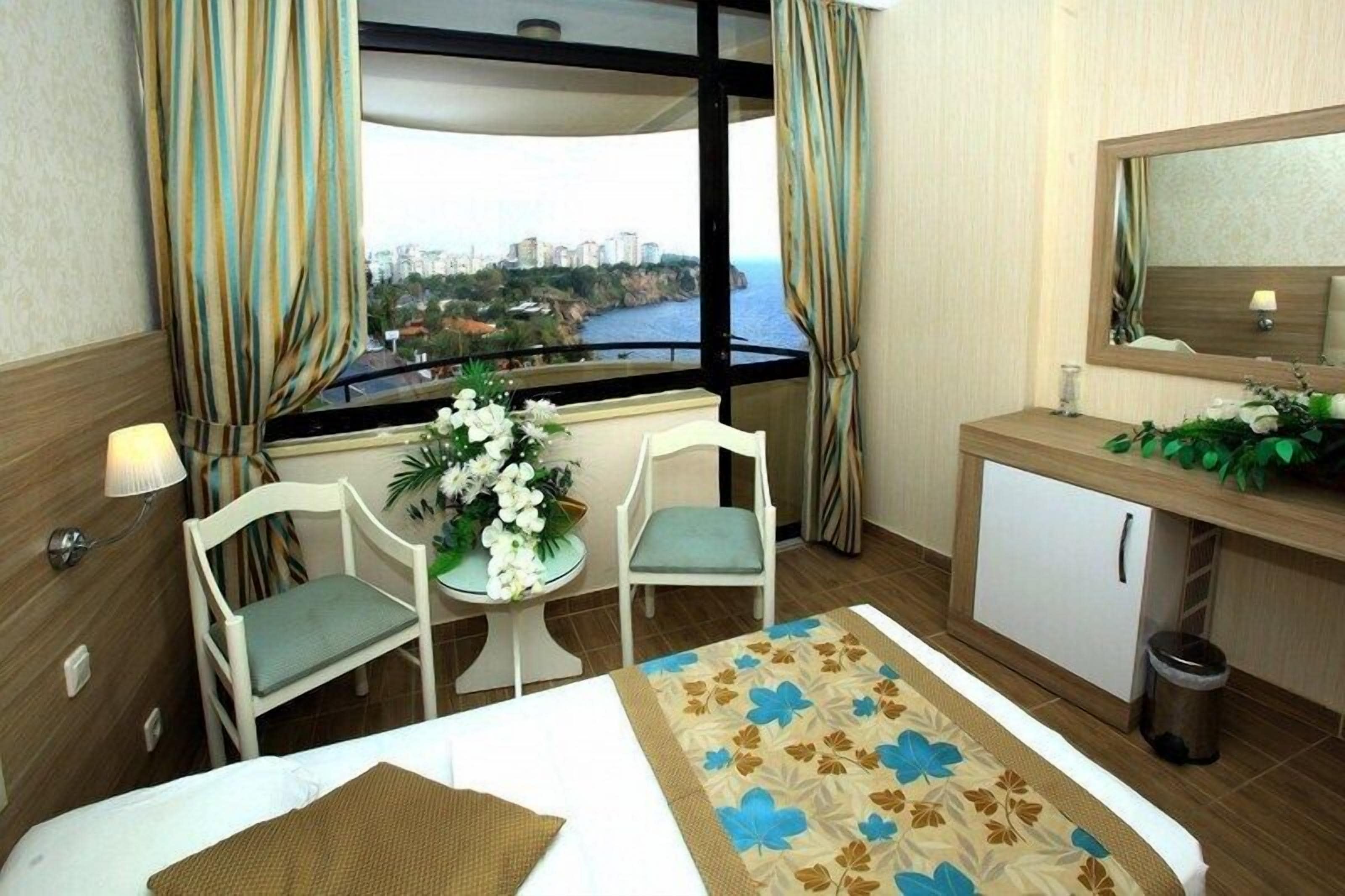 A hotel room with a bed, a small table with chairs, a bathroom with a sink and mirror, and a window with curtains.