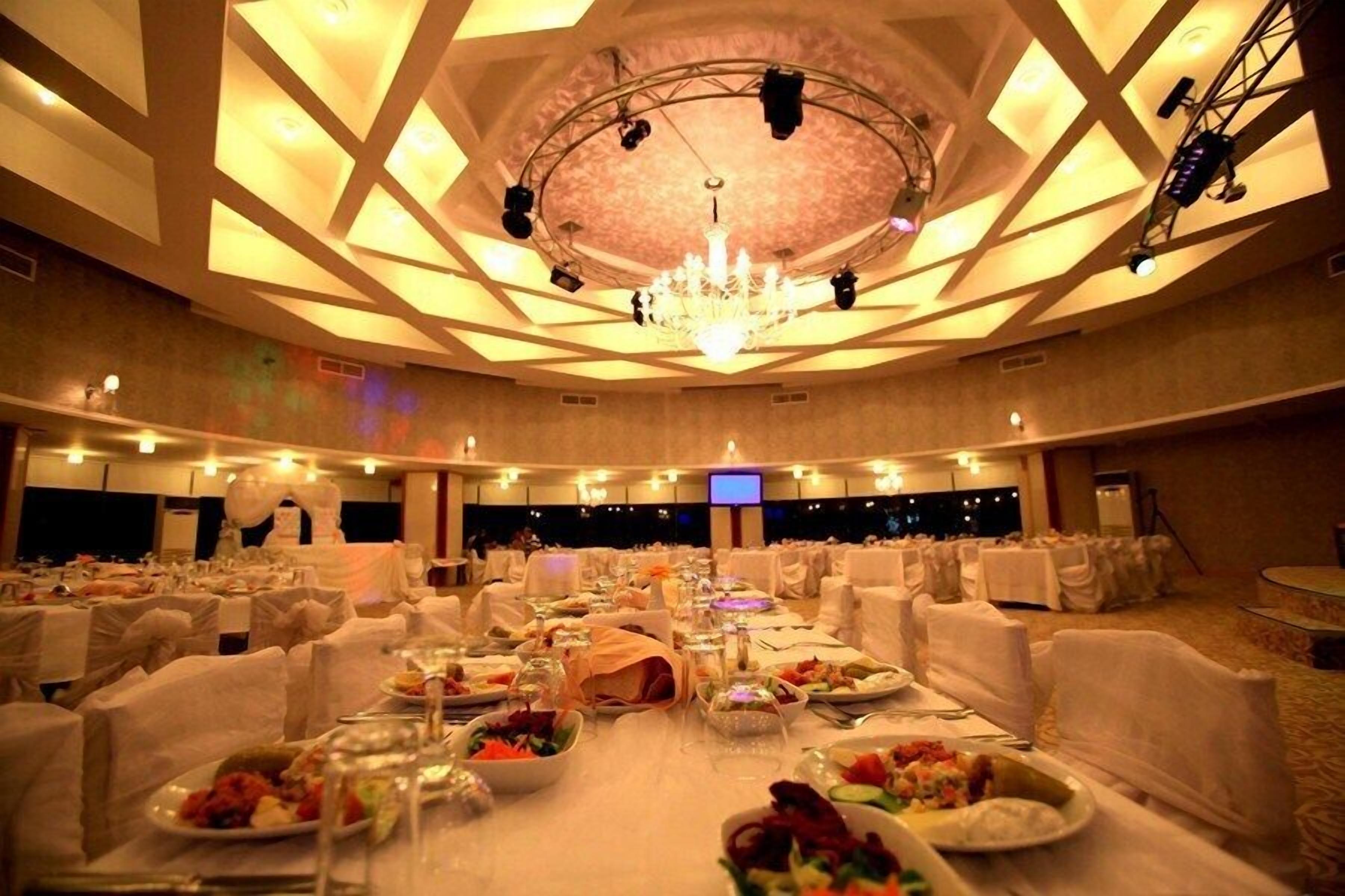 Un salón de banquetes con mesas redondas dispuestas para cenar, una araña y luces de escenario.