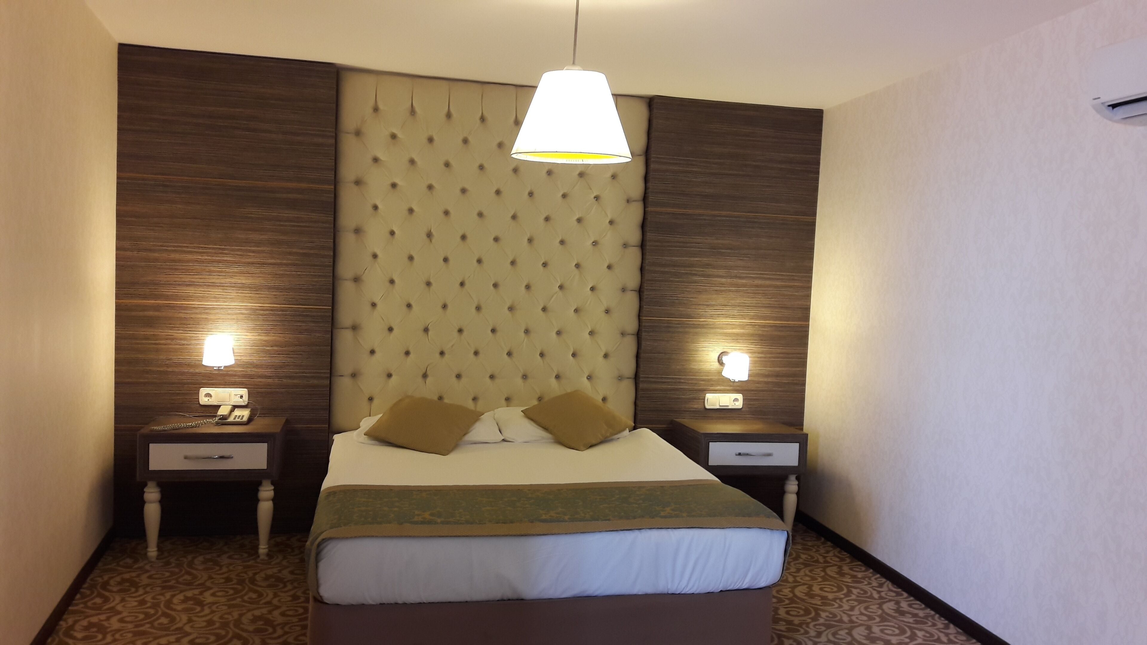 A hotel room with a large bed, two bedside tables, a hanging light fixture, and a patterned wall.