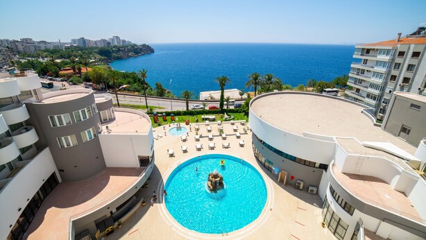 A hotel with a pool, a view of the sea, and a cityscape in the background. - Cender Hotel (Antalya)