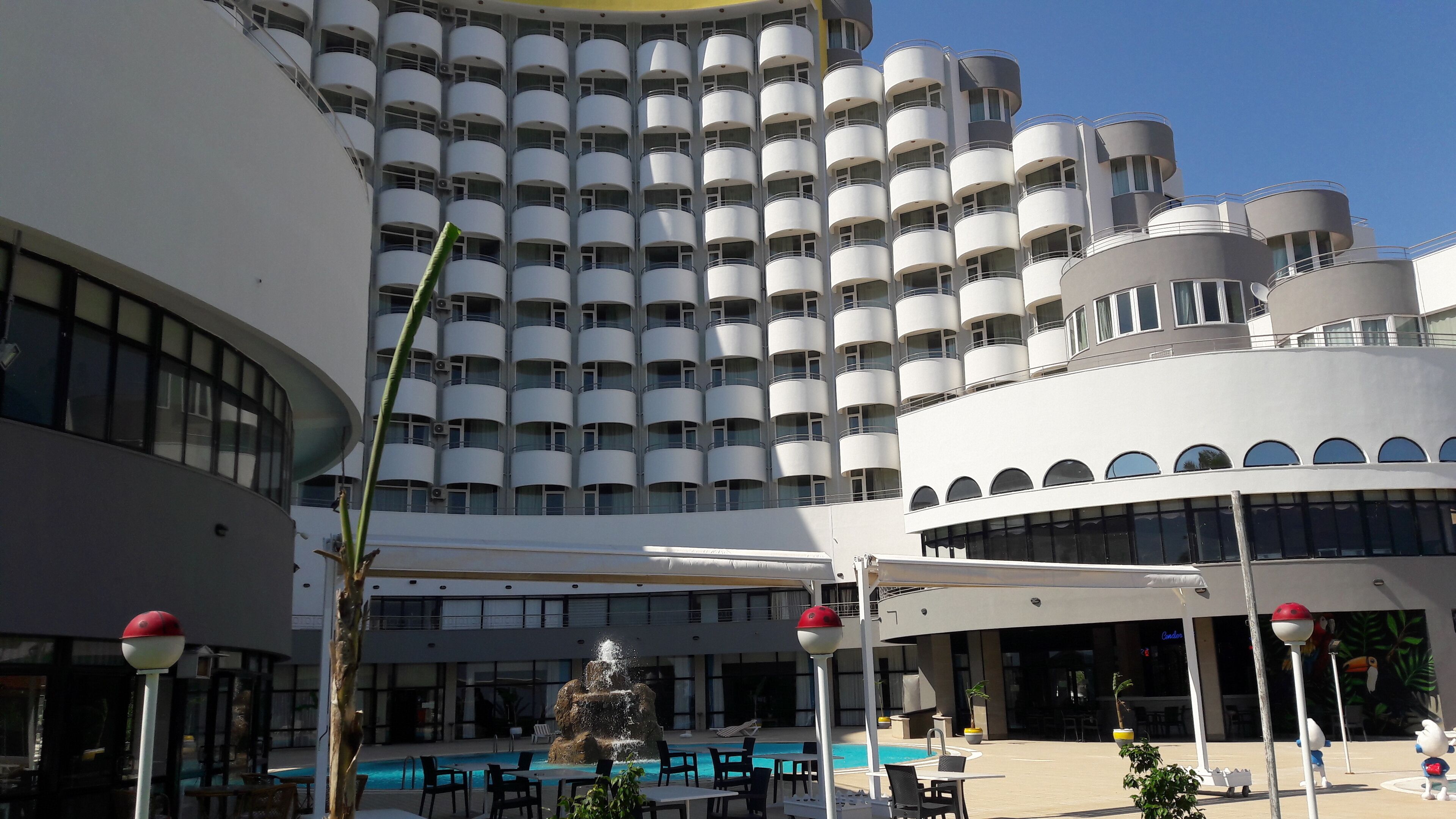 Ein modernes Hotel mit großzügigem Poolbereich, Außenbestuhlung und einer markanten, zylindrischen Bauweise.
