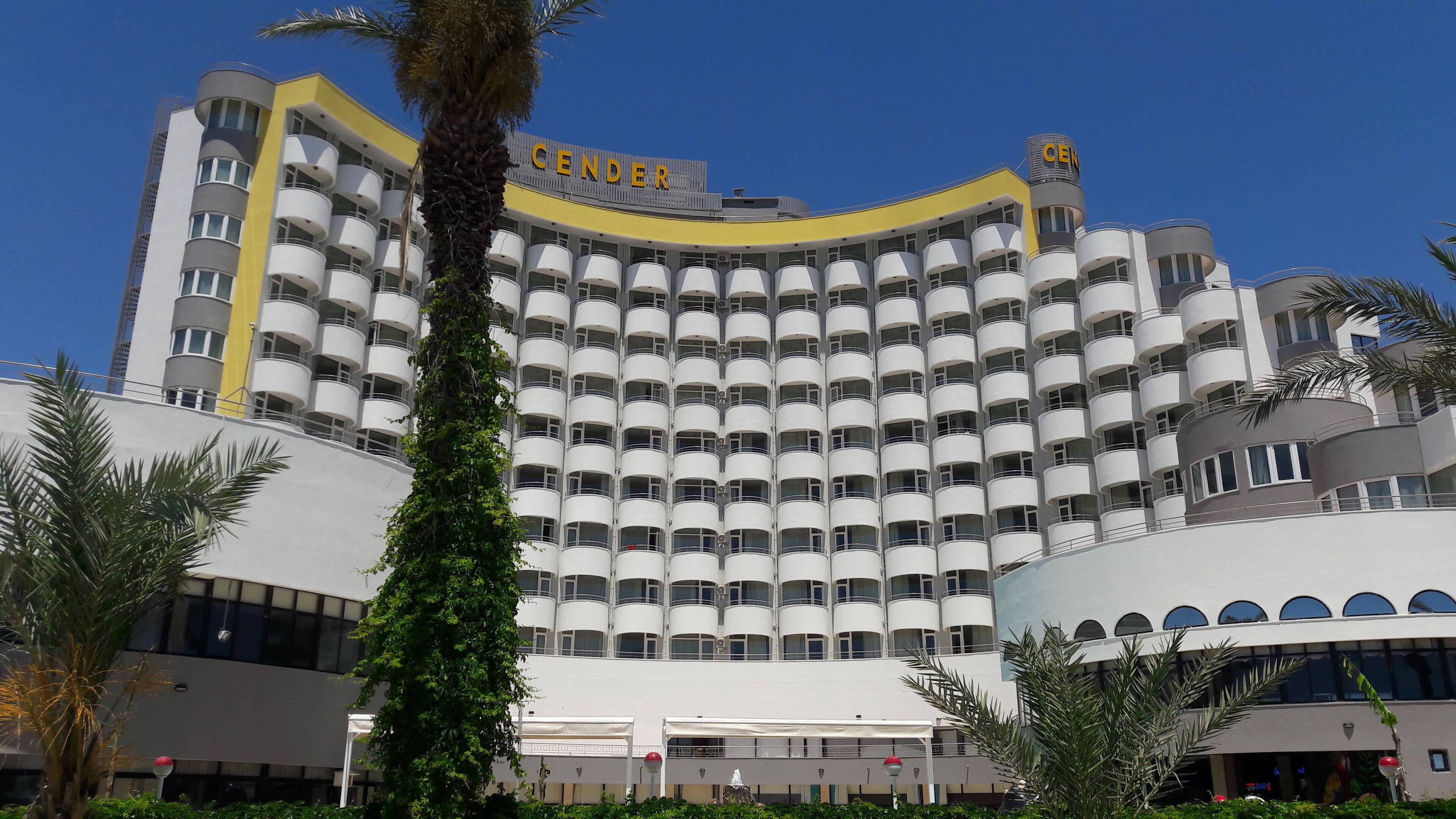 Een groot hotel met een gebogen gevel, meerdere balkons en een opvallend 'CENDER'-bord.