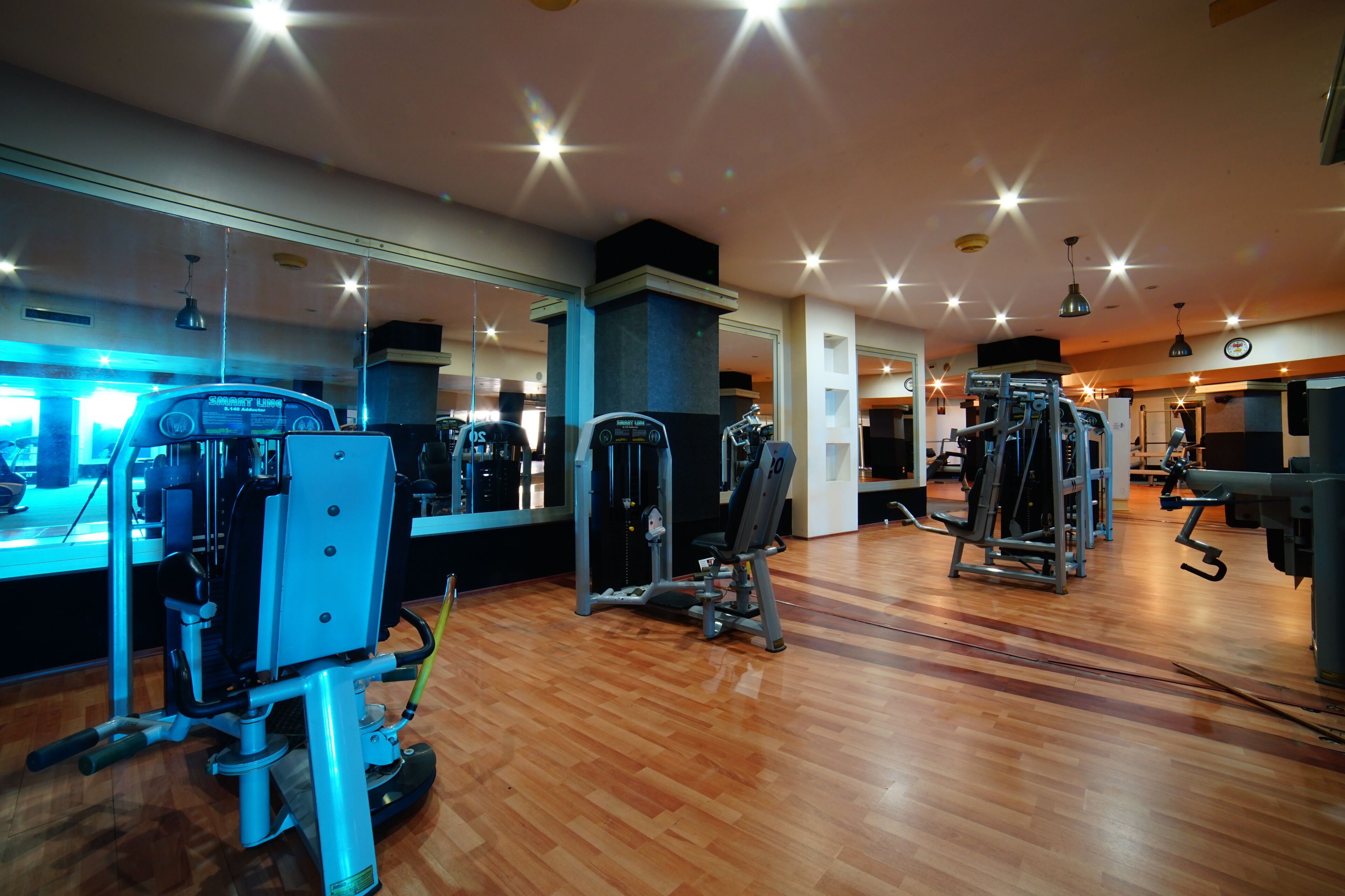 A gym with exercise machines, wooden flooring, and mirrored walls.